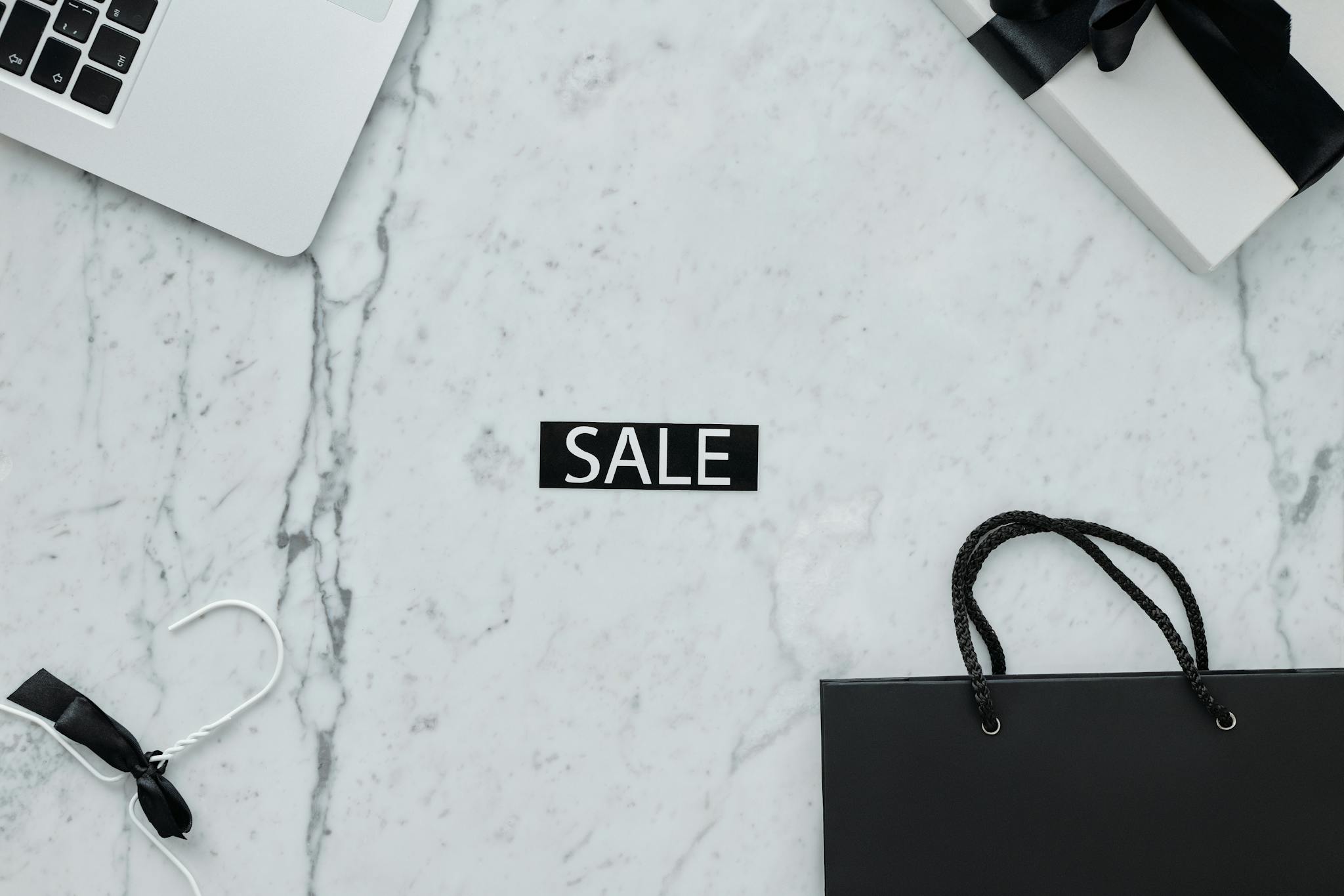 Minimalist sale-themed flat lay with laptop, gift, and shopping bag on marble.