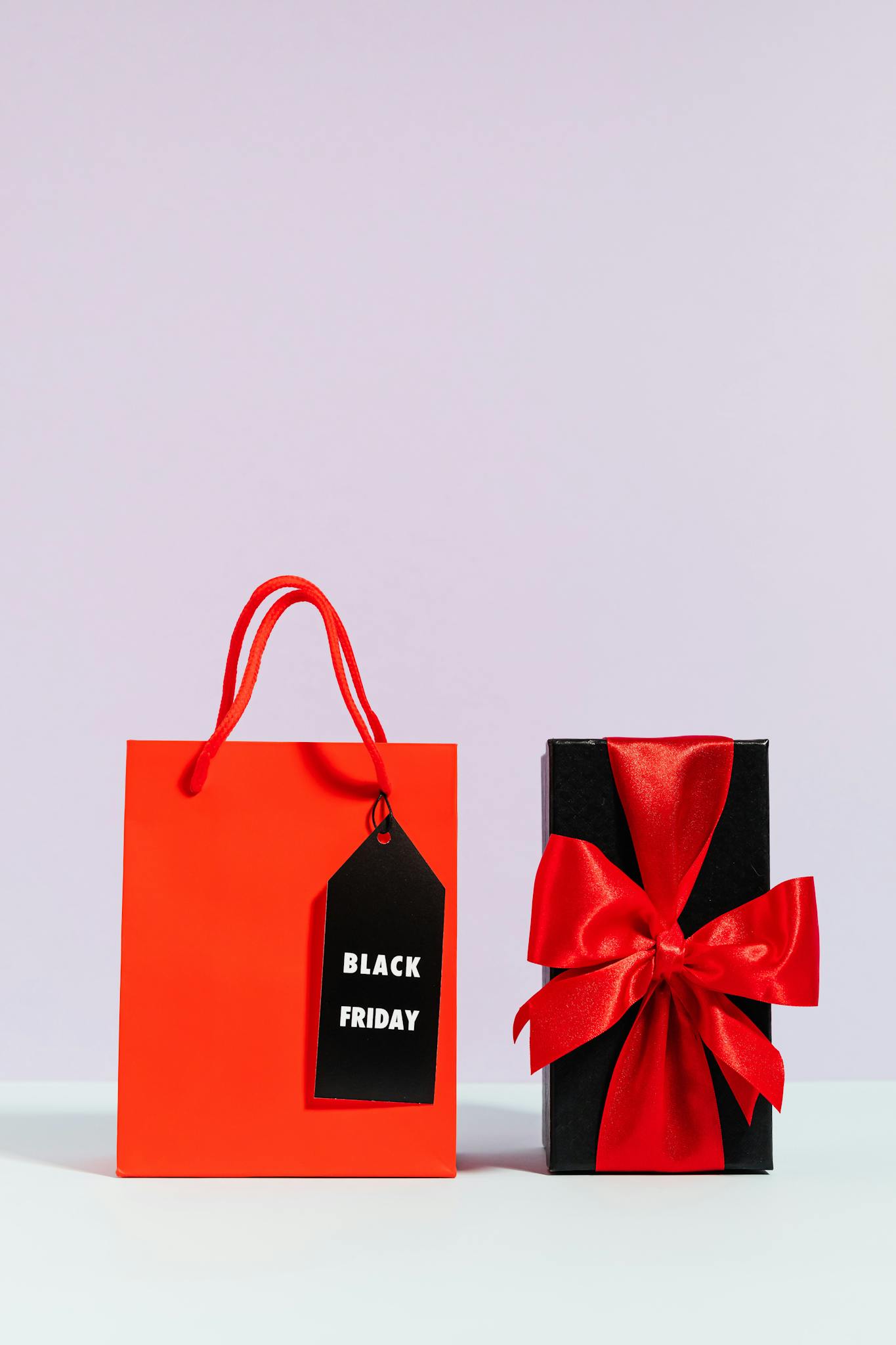 Red shopping bag and elegant gift box with red ribbon, perfect for Black Friday promotions.